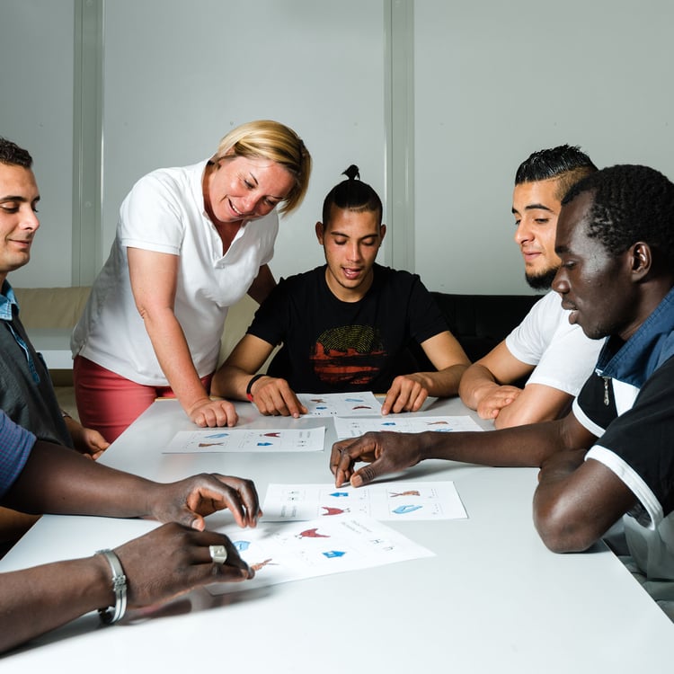 Language training for refugees in a German camp: A female German volunteer is teaching young African (Gambia) and Arabic (Algeria and Tunesia) men the German language in a refugee camp quickly errected using accomodation containers. Over 1 million refugees arrived in Germany in 2015 alone, integration of these people requires enormous efforts by the government but also by thousands of volunteers providing basic training and services for the refugees.