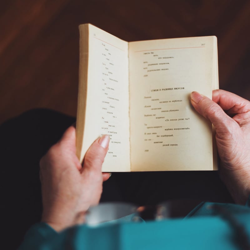 Old woman hands holding old book with russian poetry. Blurred background of soviet parquet