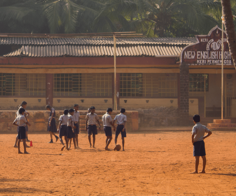 group of children playing football barefoot in a school playground in India.