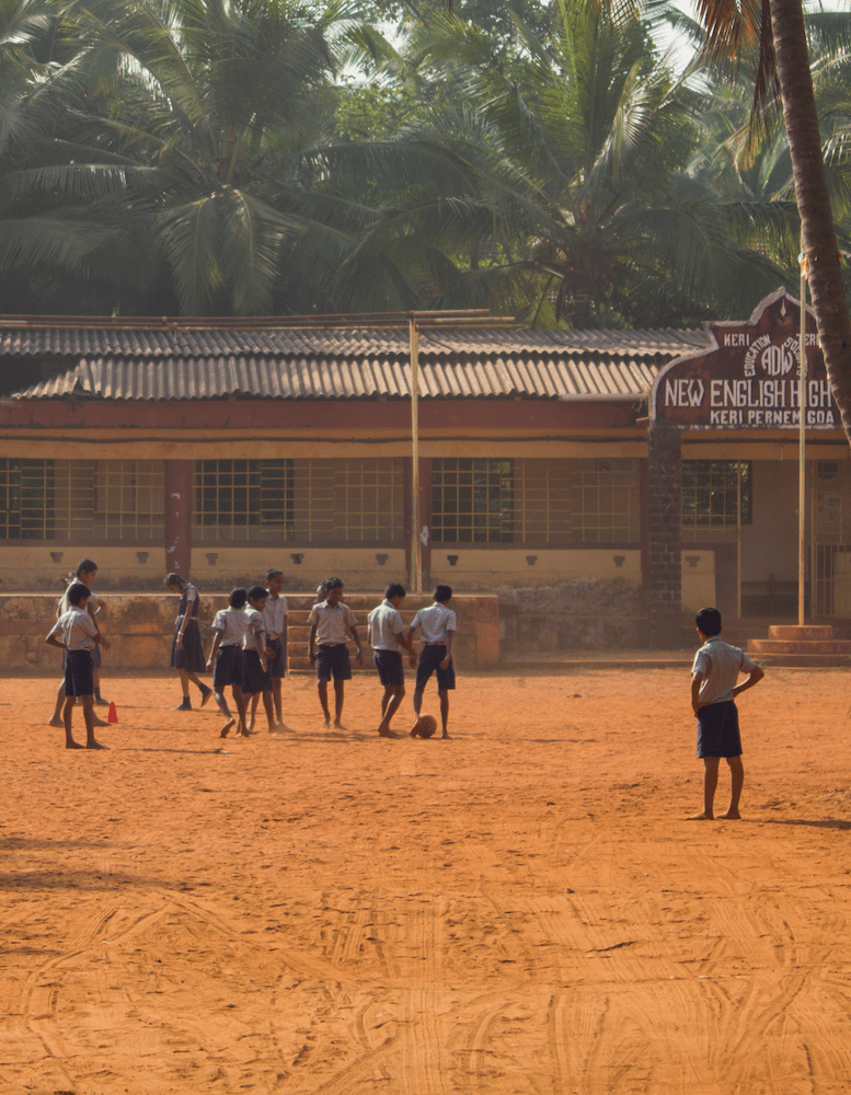 group of children playing football barefoot in a school playground in India.